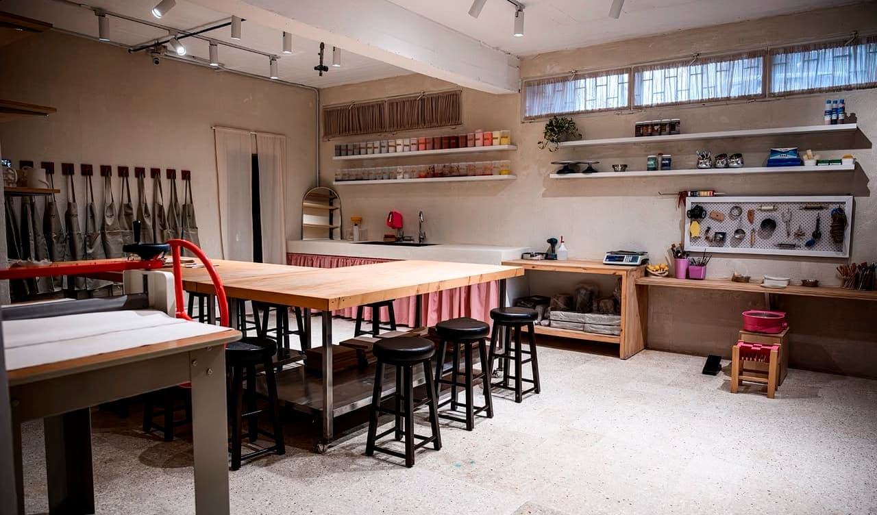 The studio: a long worktable with stools, aprons on the wall, and shelves of glazes